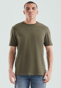 Oliwkowo-zielony t-shirt z krótkim rękawem wykonany z miękkiej bawełnianej tkaniny; posiada okrągły dekolt i małe logo "QS" na piersi.