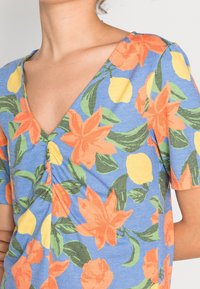 Top floral de cuello en V en azul con flores naranjas y limones amarillos. Presenta mangas cortas y un detalle fruncido en el busto. Tejido de mezcla de algodón.