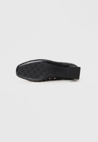 Black shoe sole with a rectangular heel. Features textured grip surface and perforated design along the sides for breathability.
