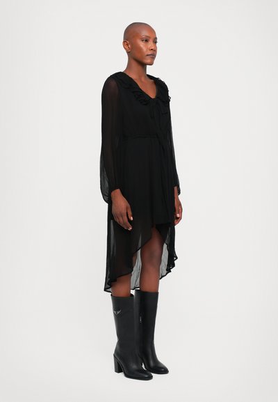 Rochie neagră din chiffon cu mâneci lungi, decolteu ondulat și tiv asimetric. Asortată cu cizme negre cu toc, până la genunchi, cu detalii accent.