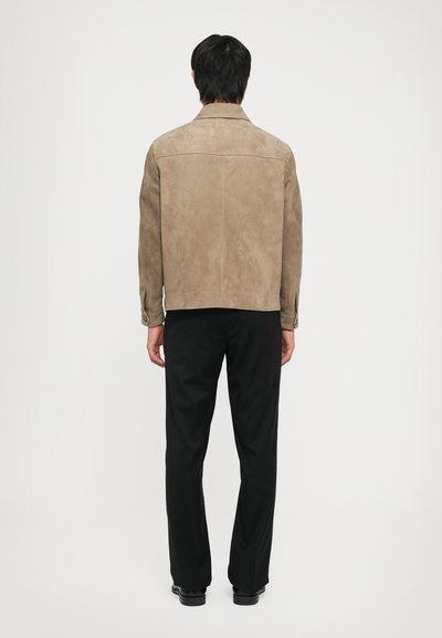 Suede beige jacket with a straight cut, folded collar, and buttoned cuffs, paired with black trousers and shoes. Clear, smooth texture.