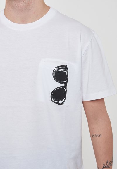 T-shirt bianco in cotone con un design di occhiali da sole stampato in nero sul taschino sinistro del petto. Collo a giro, maniche corte, tessuto texturizzato.