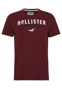 Burgundowa koszulka z okrągłym dekoltem, krótkimi rękawami, z napisem "HOLLISTER California" w białym i czarnym kolorze, z akcentem logo.