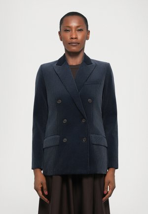 Navy corduroy double-breasted blazer with notch lapels, two front pockets, and six black buttons, paired with a dark dress.