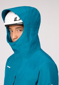 Türkise Kapuzenjacke mit einem schlanken Design, hergestellt aus leichtem Material. Verfügt über einen hohen Kragen und eine Reißverschlusstasche, geeignet für den Außeneinsatz.