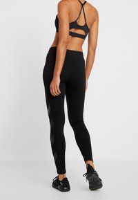Set di abbigliamento attivo nero composto da un reggiseno sportivo con un design a taglio e leggings neri con dettagli a striscia riflettente, realizzati in tessuto elasticizzato.