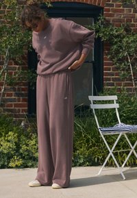 Hanorac supradimensionat, mov, cu detaliu brodat "self.", asortat cu pantaloni largi, realizați dintr-un material moale și texturat.