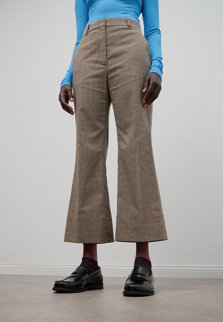 Brązowe, w kratkę szerokie spodnie z wysokim stanem, wykonane z teksturowanej tkaniny. Noszone z czarnymi mokasynami i bordowymi skarpetkami.
