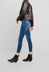 Veste en cuir texturé marron, jean skinny bleu et bottines noires. Le design des bottines présente un petit talon et un ribbed vertical.