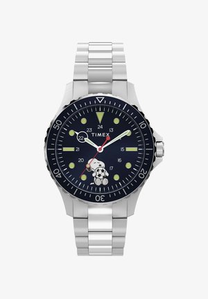 Montre Timex en métal argenté avec cadran noir, aiguilles lumineuses, lunette tournante et Snoopy tenant un ballon de football à la position 6 heures.