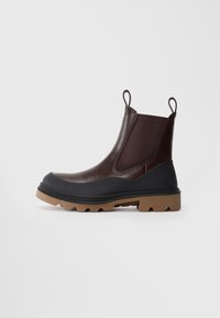 Bottes Chelsea marron avec panneaux latéraux en élastique, bout en caoutchouc noir, semelle en caoutchouc texturée et languettes au talon pour un enfilage facile.