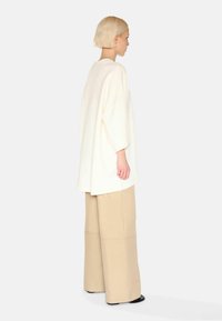 Bílý oversize top s nízkými rameny, spojený s béžovými kalhotami s širokými nohavicemi. Hladká tkanina, minimální design a neutrální barvy.