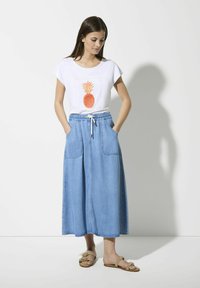 Witte T-shirt met een oranje ananasgrafiek, gecombineerd met een lichtblauwe denimrok met elastische tailleband en twee voorzakken.