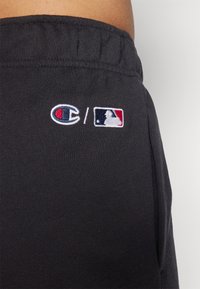 Čierne bavlnené teplákové nohavice majú elastický pás a výšivky loga Champion a MLB v farbách červenej, bielej a modrej.