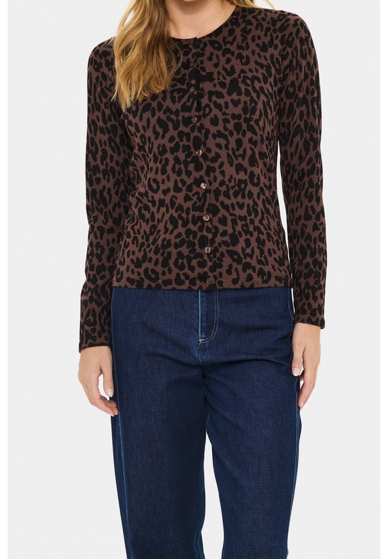 Femme portant un cardigan boutonné à manches longues imprimé léopard marron et noir, associé à un jean taille haute bleu foncé.