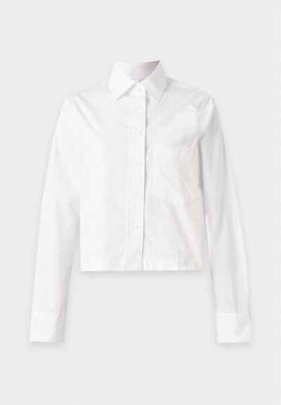 Chemise blanche à manches longues avec boutons, col et poche poitrine, présentée à plat sur un fond gris clair.