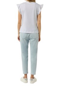 White short-sleeve top with ruffled sleeves, paired with light blue high-waisted jeans and white sneakers with silver accents.