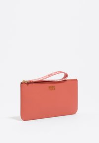 Bolso de cuero coral con acabado texturizado, herrajes dorados y correa de muñeca de tela con estampado. Presenta el logo grabado en la parte frontal.