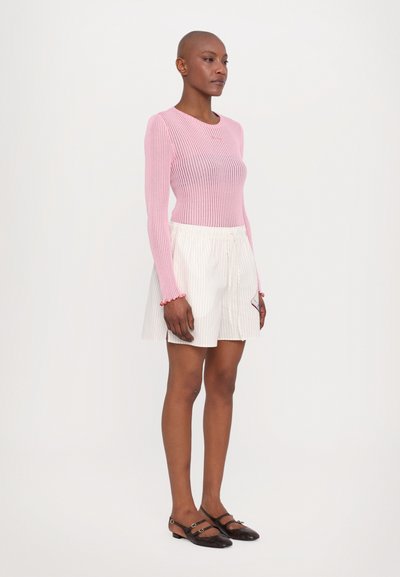 Lys rosa ribbet langermet topp, hvite plisserte shorts, brune sko med stroppdetaljer. Enkel design, tettsittende topp, avslappet stil.