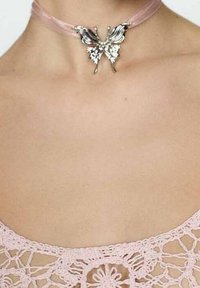 Collar de cinta rosa con un colgante de mariposa plateada que presenta alas intrincadas y detalles de hojas, llevado sobre una blusa de encaje de color claro.