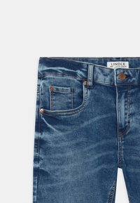 Jeans en denim bleu avec bouton avant, passants de ceinture et deux poches avant, y compris une petite poche à monnaie, présentés à plat sur un fond blanc.