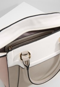 Gestructureerde handtas met witte, beige en blushpanelen; gladde leren textuur; gouden hardware; binnenzak met rits zichtbaar.
