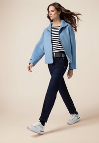 Chaqueta con cremallera de gran tamaño en azul claro; camisa de manga larga ajustada a rayas; vaqueros oscuros; zapatillas blancas con detalles en plata.