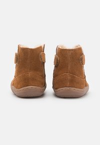 Botas de tobillo de ante marrón con un suave forro de piel de conejo, correas de velcro en los lados y una suela de goma con un patrón texturizado.