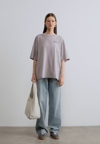 Light purple oversized t-shirt with short sleeves, paired with light blue baggy jeans. Model holds a cream-colored shoulder bag.
