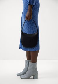 Black leather shoulder bag with embossed circular design, paired with a ribbed blue dress and light gray ankle boots. Smooth texture, medium size.