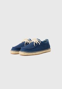 Espadrilles en toile marine avec des lacets beiges, bout rond et semelle en jute tressé, présentant un dessus texturé et une doublure intérieure contrastante.
