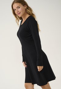 Abito nero a maniche lunghe con scollatura a barca, orlo svasato e superficie liscia. Il design semplice ne esalta la versatilità per varie occasioni.