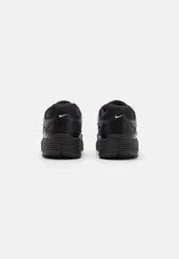 Baskets de sport noires avec un dessus en maille, une semelle en caoutchouc texturée et un célèbre swoosh blanc de Nike au niveau du talon. Vue arrière affichée.