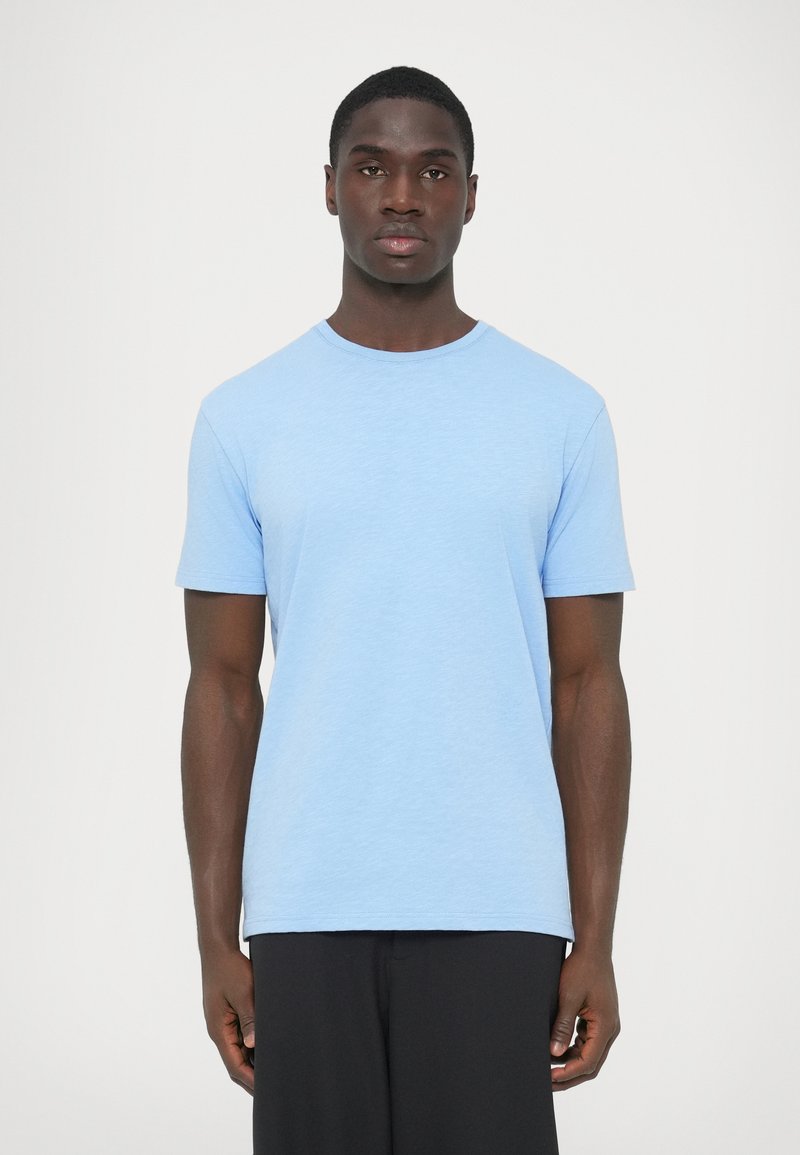 Μπλε βαμβακερό t-shirt με κοντά μανίκια, στρογγυλή λαιμόκοψη και ελαφρώς υφασμάτινη υφή. Απλός σχεδιασμός, ευθεία γραμμή, συνδυασμένο με μαύρο παντελόνι.