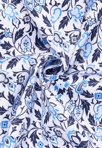 Tessuto di cotone con sfondo bianco, caratterizzato da un motivo floreale blu e accenti blu scuro, arrotolato per mostrare la texture e i dettagli del design.