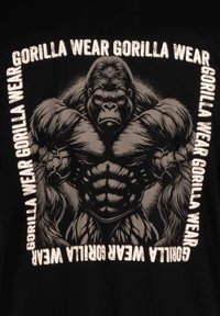 T-shirt noire avec un graphisme de gorille musclé, portant le texte "GORILLA WEAR" en blanc gras autour du design. Illustration et texture détaillées.