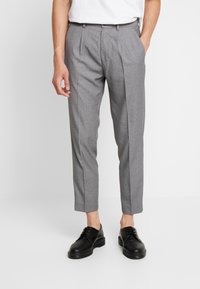 Grå skräddarsydda byxor med texturerad yta, två framvikningar, något kortare längd, kombinerade med blanka svarta skor.