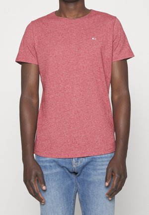 Rød t-shirt med korte ærmer, lavet af et struktureret stof med rund hals; har et lille logo på venstre bryst. Kombineret med blå jeans.