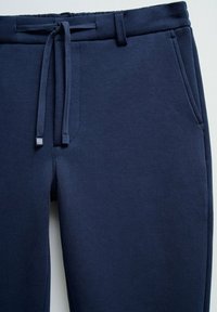 Pantalones de chándal azul marino hechos de material suave, con cinturilla elástica, cordón y bolsillos laterales. Textura suave, sin patrones ni acentos.