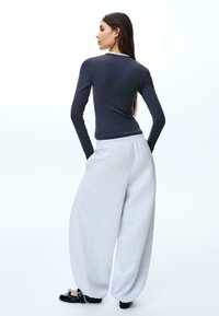 Crna majica dugih rukava i sive oversized dukserice, izrađene od glatkog materijala, opuštenog kroja s manžetama na nogavicama. Crne cipele upotpunjuju izgled.