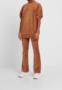 Survêtement en velours côtelé marron comprenant un col roulé ample et un pantalon évasé. Présente une texture côtelée et un petit logo sur la poitrine.