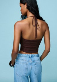 Smeđi krošej halter crop top s dizajnom vezivanja na leđima, uparen s svijetloplavim trapericama visokog struka koje imaju stražnje džepove.