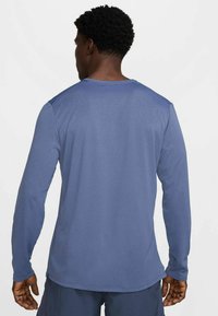 Langarmshirt in einfarbigem Marineblau aus glattem Material. Verfügt über einen Rundhalsausschnitt und figurbetonte Ärmel mit leicht verlängertem Rückenteil.