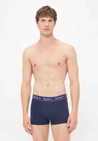 Marineblaue Baumwoll-Boxershorts mit einem Logo-Bund, die eine enganliegende Passform und eine glatte Textur bieten, präsentiert an einem Modell vor einem neutralen Hintergrund.