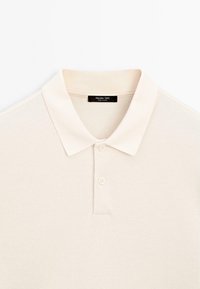 Cremfarbener Polo-Shirt mit kurzärmligen, zwei Knöpfen und einem schwarzen Etikett mit der Aufschrift "Massimo Dutti" im Kragen.