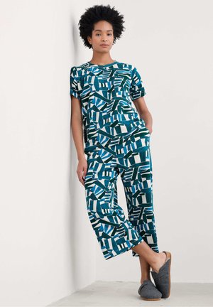 Teal-musterndes Loungewear-Set bestehend aus einem kurzärmeligen Oberteil und einer verkürzten Hose mit abstrakten Formen. Der Stoff wirkt weich, leicht und bequem.