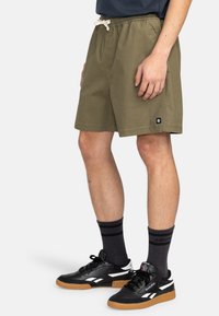 Olivgrüne Baumwollshorts mit elastischem Bund und Kordelzug, Seitentaschen und einem kleinen Logoschild am Saum.