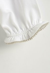 Tessuto bianco con un polsino in elastico arricciato all'orlo, caratterizzato da una decorativa rifinitura dorata di piccole perline circolari lungo il bordo.