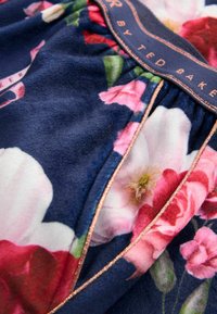 Navy floral fabric featuring pink and white flowers, soft texture, gathered design with rose gold trim along the edges, and branding label visible.