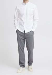 Hvid skjorte med ståkrave, enkelt brystlomme; parret med grå joggerbukser og hvide sneakers. Glat stof, afslappet pasform.
